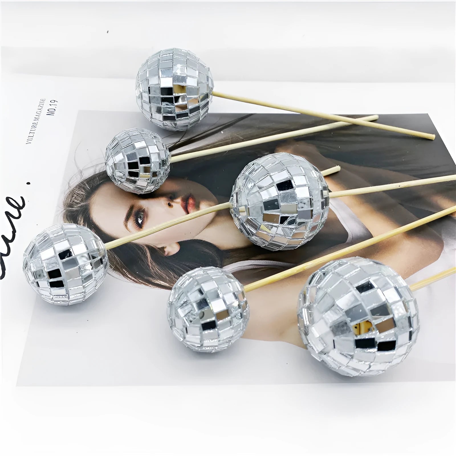 Glass mirror disco ball cake decoration on a wooden stick, showing reflective surface.
