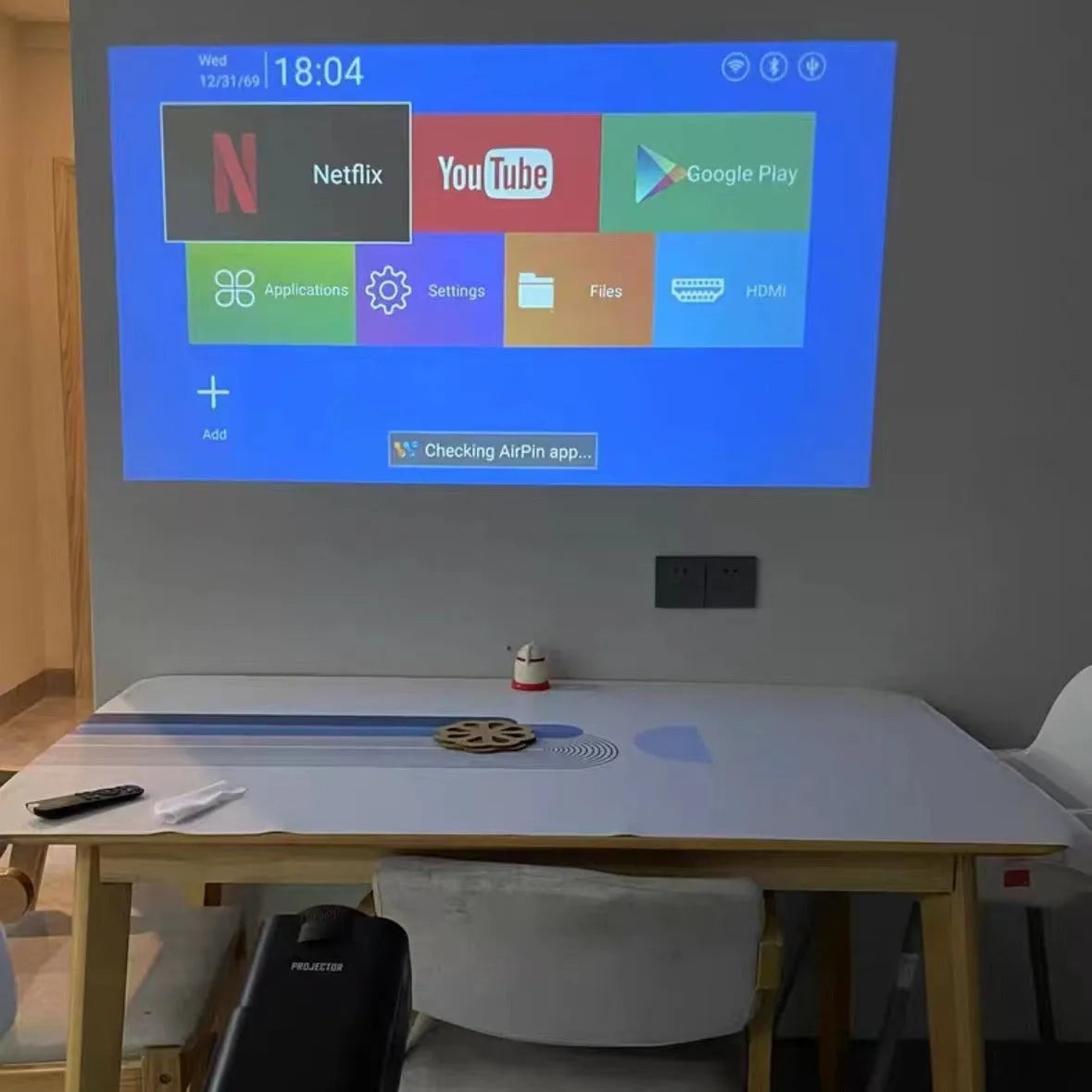 A white home projector unit on a wooden surface, showcasing its lens and wireless capabilities for HD projection.