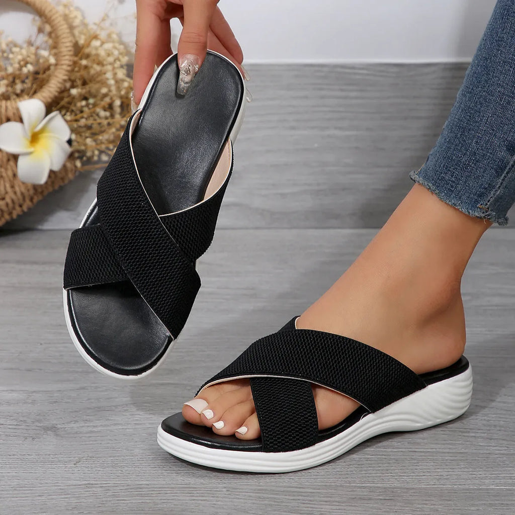 Black women's wedge slippers with cross-strap and thick rubber sole, showing peep-toe design
