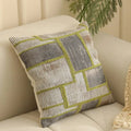 Square jacquard cushion cover with woven floral pattern on a grey sofa, showing zip closure and textured fabric.