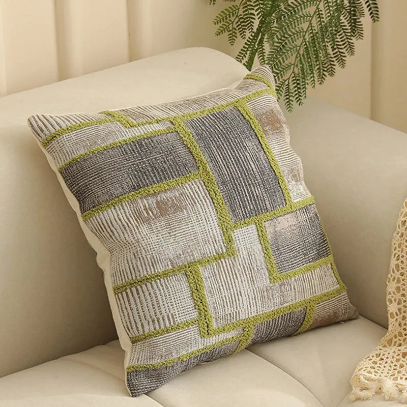 Square jacquard cushion cover with woven floral pattern on a grey sofa, showing zip closure and textured fabric.