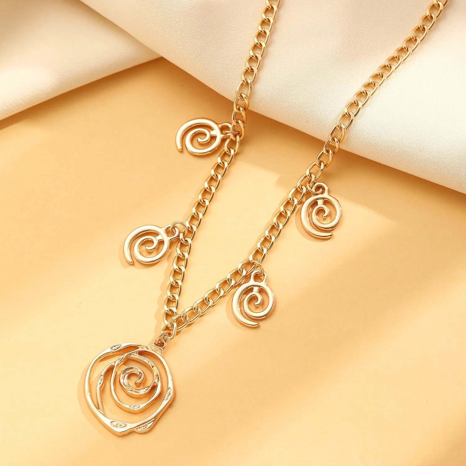 Gold spiral donut necklace, bracelet, and ear hooks set for women on a plain background.