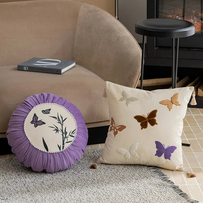 Square decorative cushion with embroidered butterfly pattern in beige, black, or purple colours.