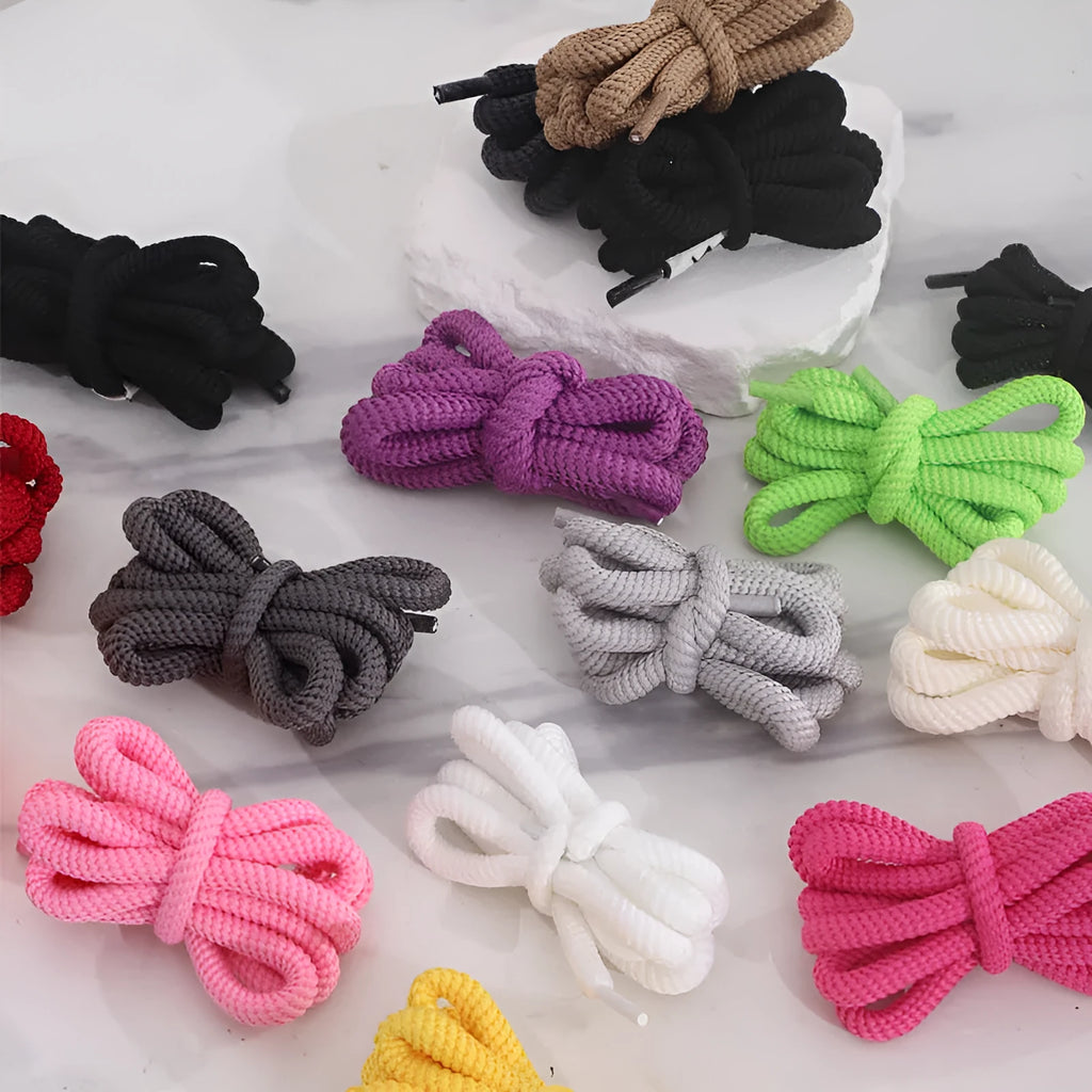 A pair of black oval shoelaces with round profile next to colour swatches showing pink, blue, gray, and orange options.