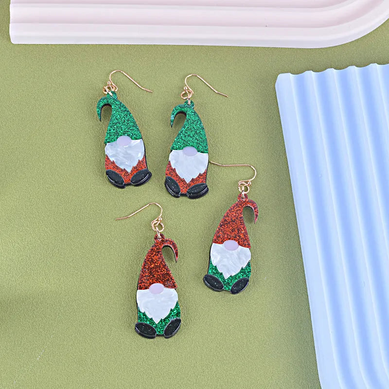 Close-up of a pair of Santa Claus cartoon acrylic earrings in red, green, and red-and-green hat designs on a light background