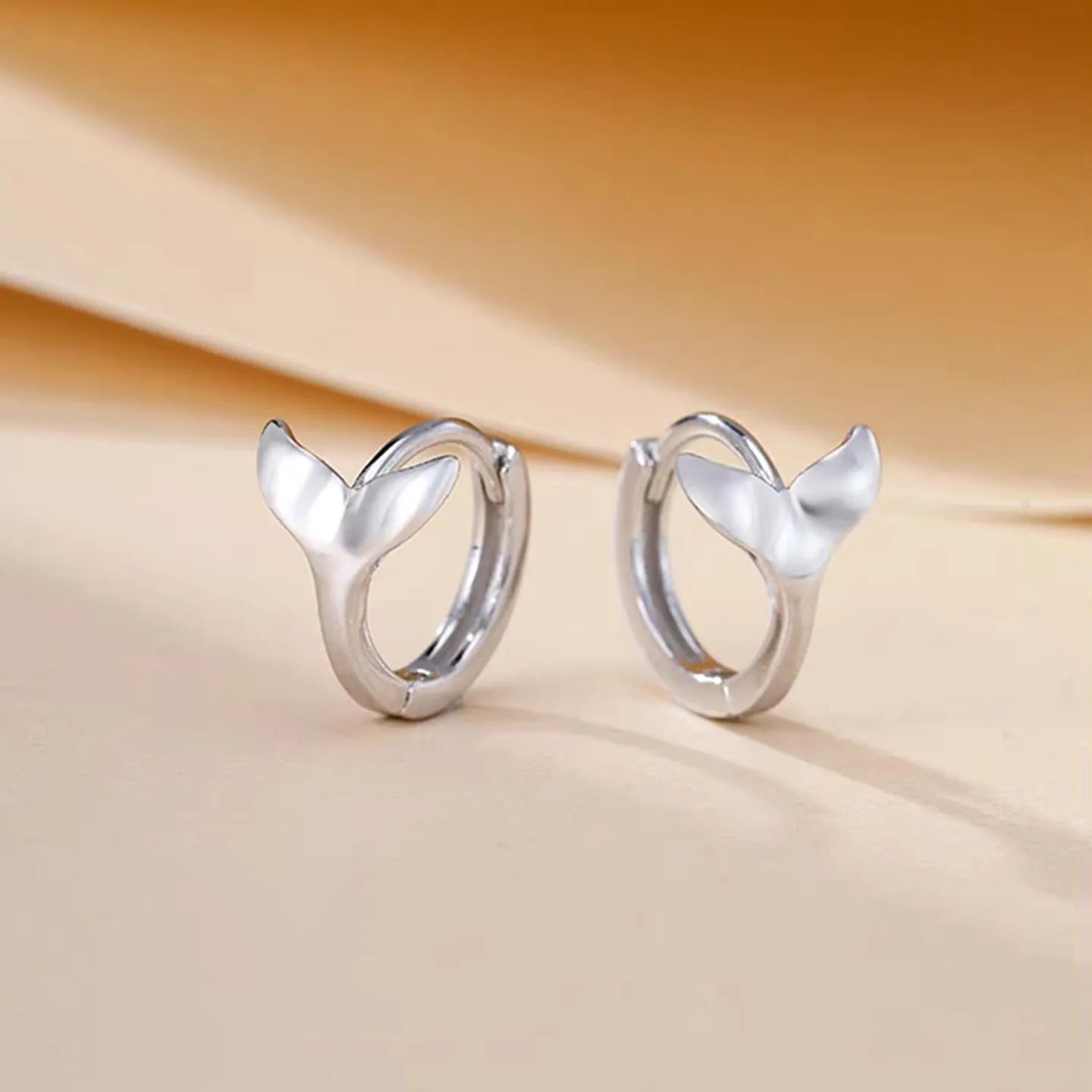 A pair of simple women's fishtail earrings with an electroplated finish in white gold or yellow gold colour.