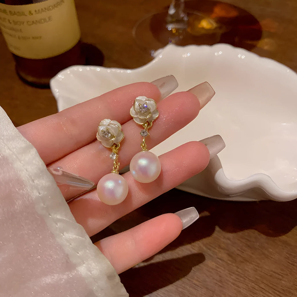 Close-up of women's alloy camellia flower stud earrings with a pearl detail on a white background.