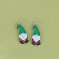 Close-up of a pair of Santa Claus cartoon acrylic earrings in red, green, and red-and-green hat designs on a light background