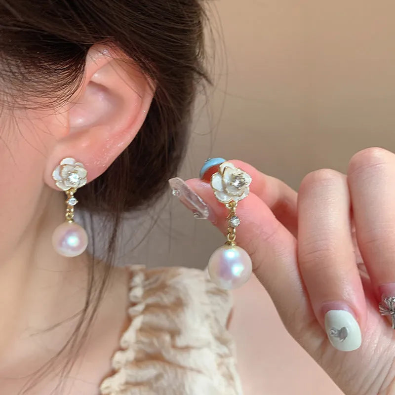 Close-up of women's alloy camellia flower stud earrings with a pearl detail on a white background.