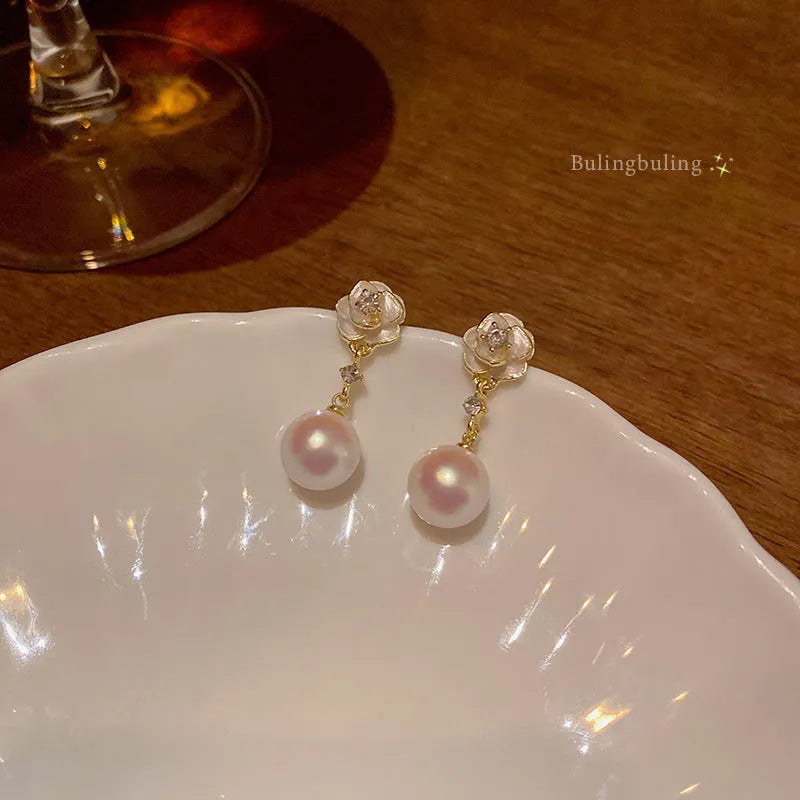 Close-up of women's alloy camellia flower stud earrings with a pearl detail on a white background.
