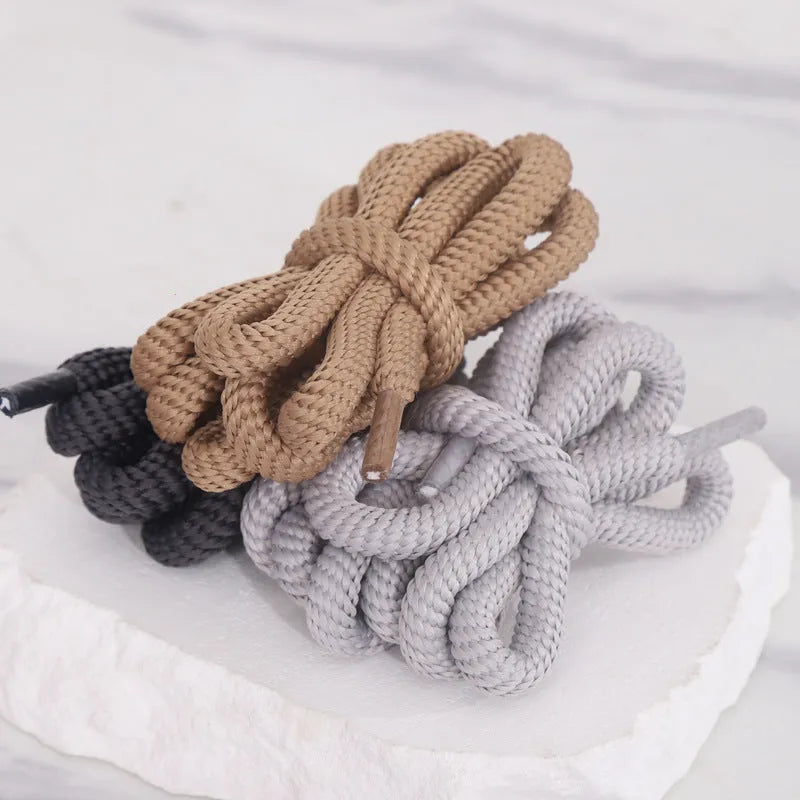 A pair of black oval shoelaces with round profile next to colour swatches showing pink, blue, gray, and orange options.