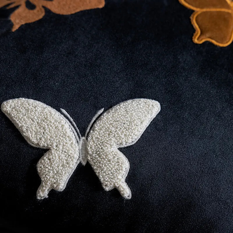 Square decorative cushion with embroidered butterfly pattern in beige, black, or purple colours.