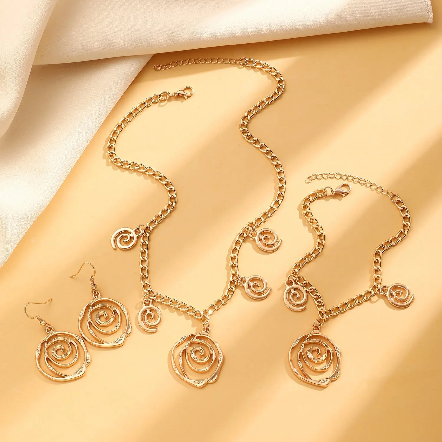Gold spiral donut necklace, bracelet, and ear hooks set for women on a plain background.