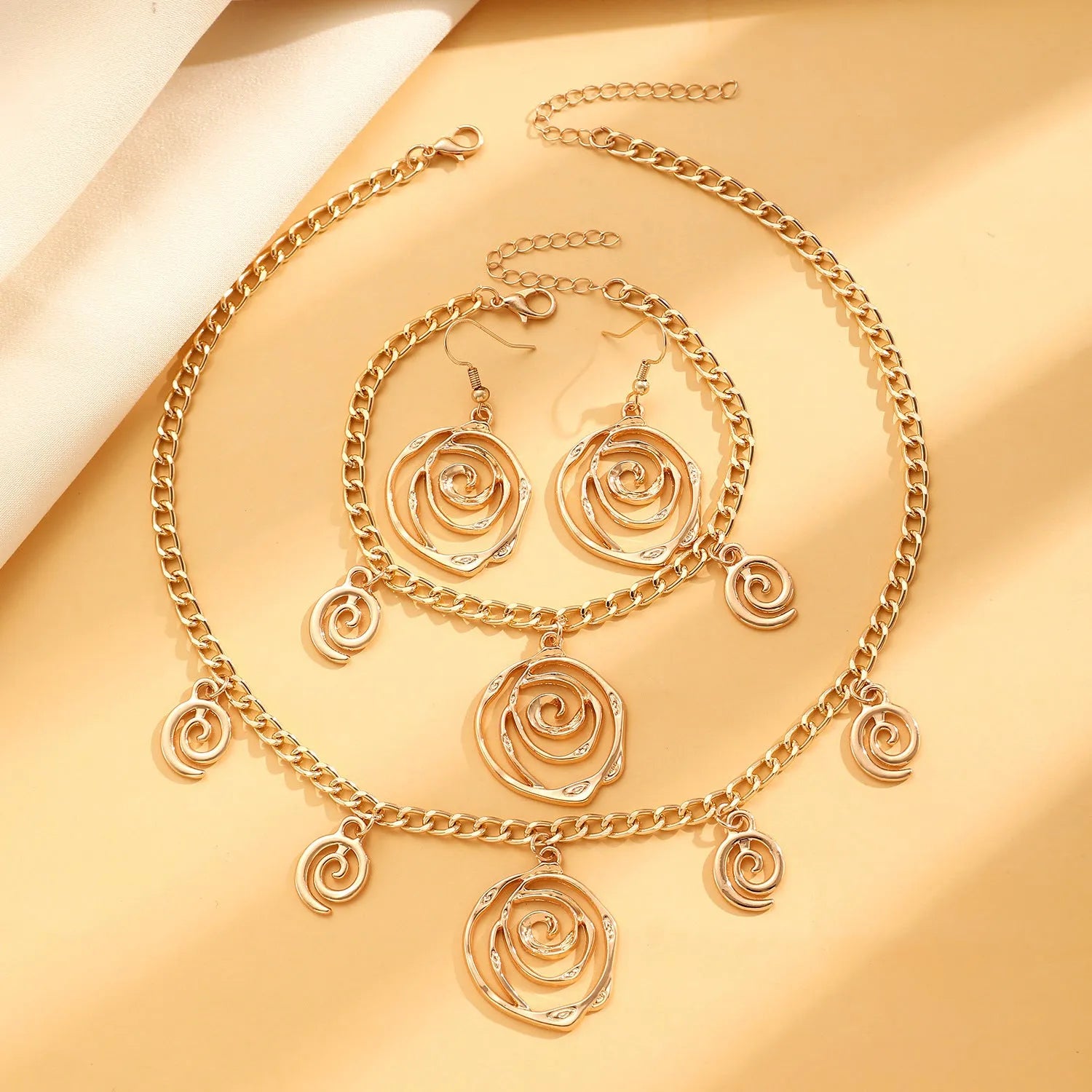 Gold spiral donut necklace, bracelet, and ear hooks set for women on a plain background.