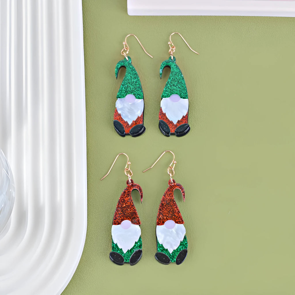 Close-up of a pair of Santa Claus cartoon acrylic earrings in red, green, and red-and-green hat designs on a light background