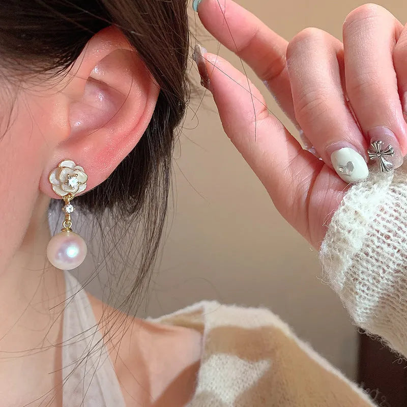 Close-up of women's alloy camellia flower stud earrings with a pearl detail on a white background.