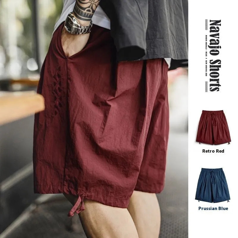 Men's loose Prussian Blue nylon shorts with embroidery on a beach background.