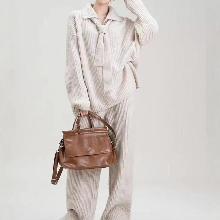 Dark gray knitted sweater and trousers two-piece set laid flat, showing long sleeves and elegant stitching details.