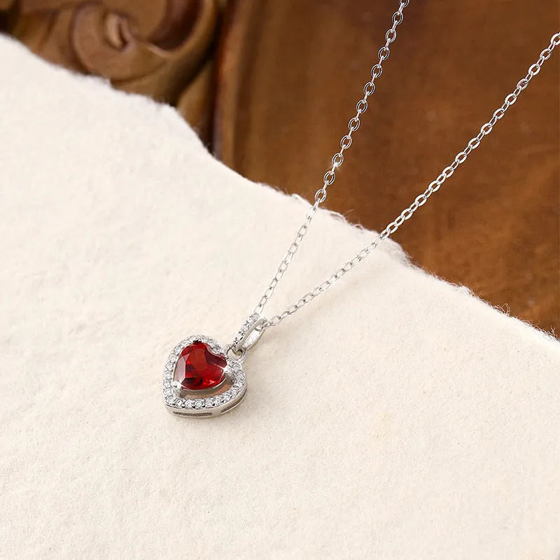 Sterling silver heart pendant necklace with inlaid gemstone on a cross chain, adjustable length.