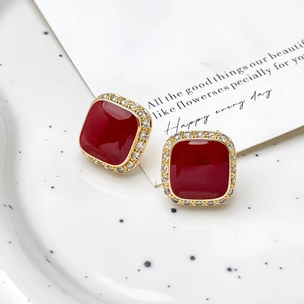 A pair of red geometric square alloy earrings with inlaid detailing on a white background.