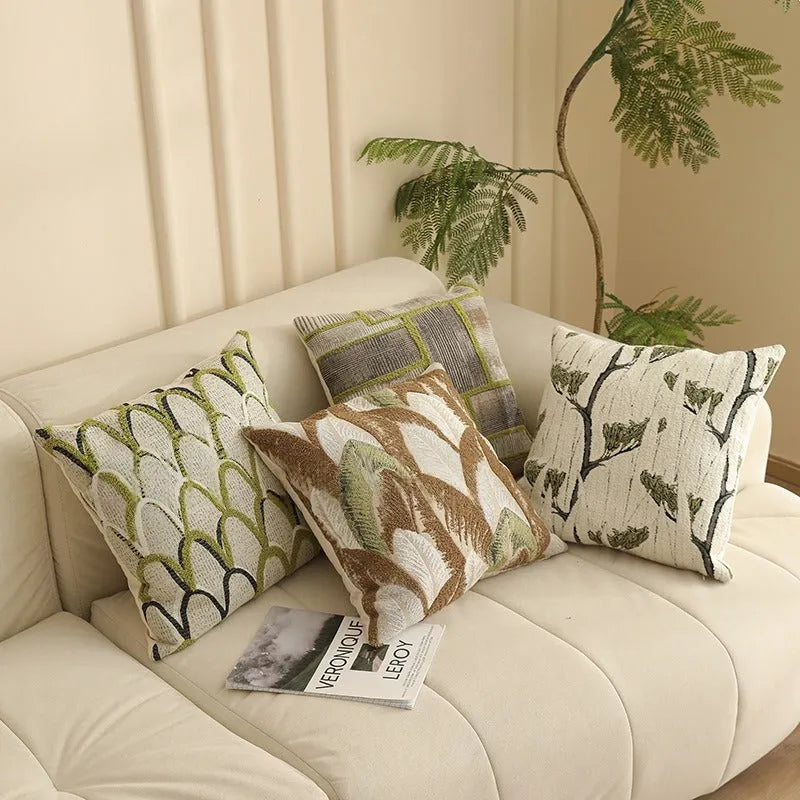 Square jacquard cushion cover with woven floral pattern on a grey sofa, showing zip closure and textured fabric.