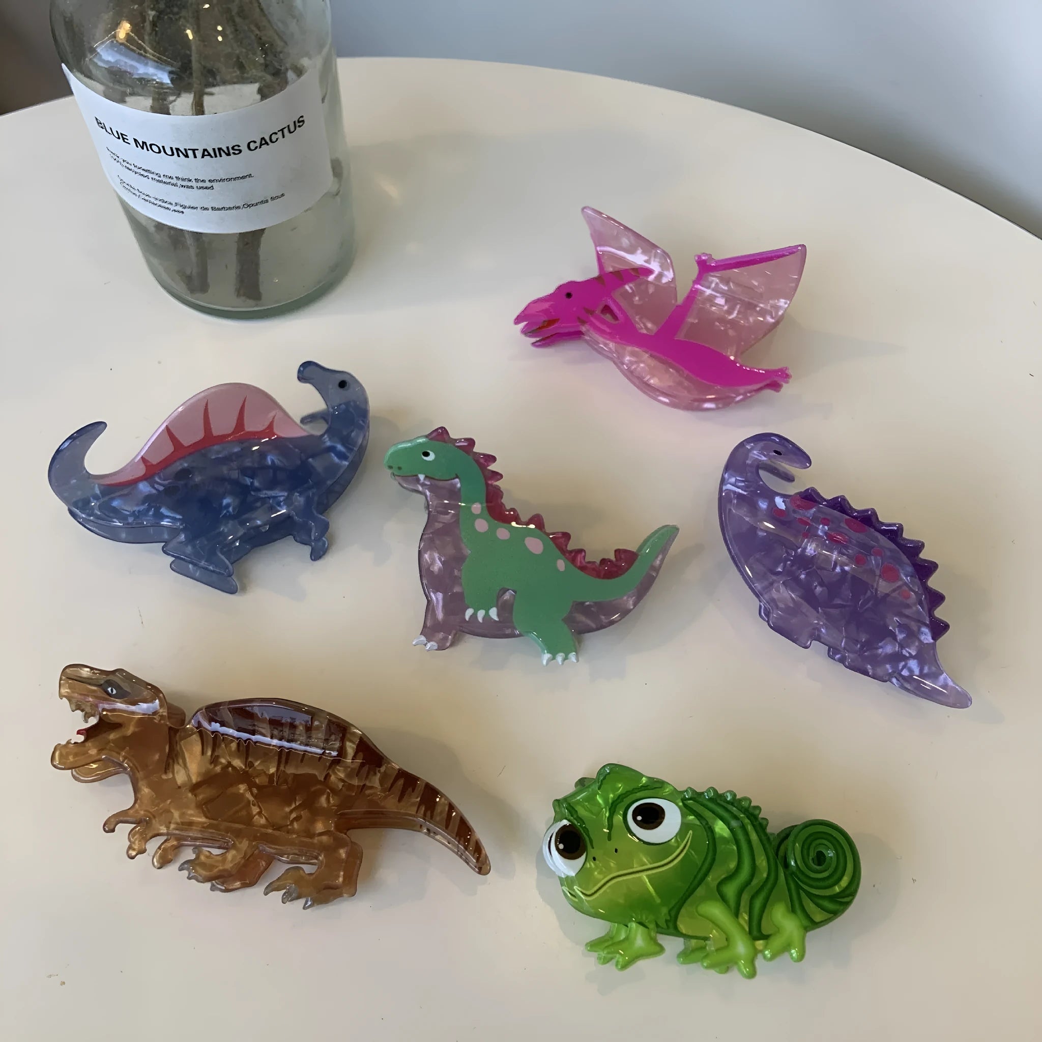 Dinosaur acrylic jaw clip hairpin in six colours including pink pterosaur and green stegosaurus on neutral background