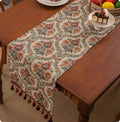 Long decorative table runner with tassels on a wooden dining table in a blue ginkgo leaf pattern.