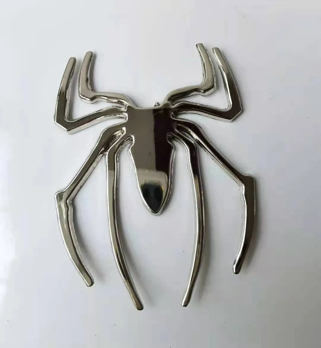 Three-dimensional metal spider bumper sticker in metallic finish on a car bumper.