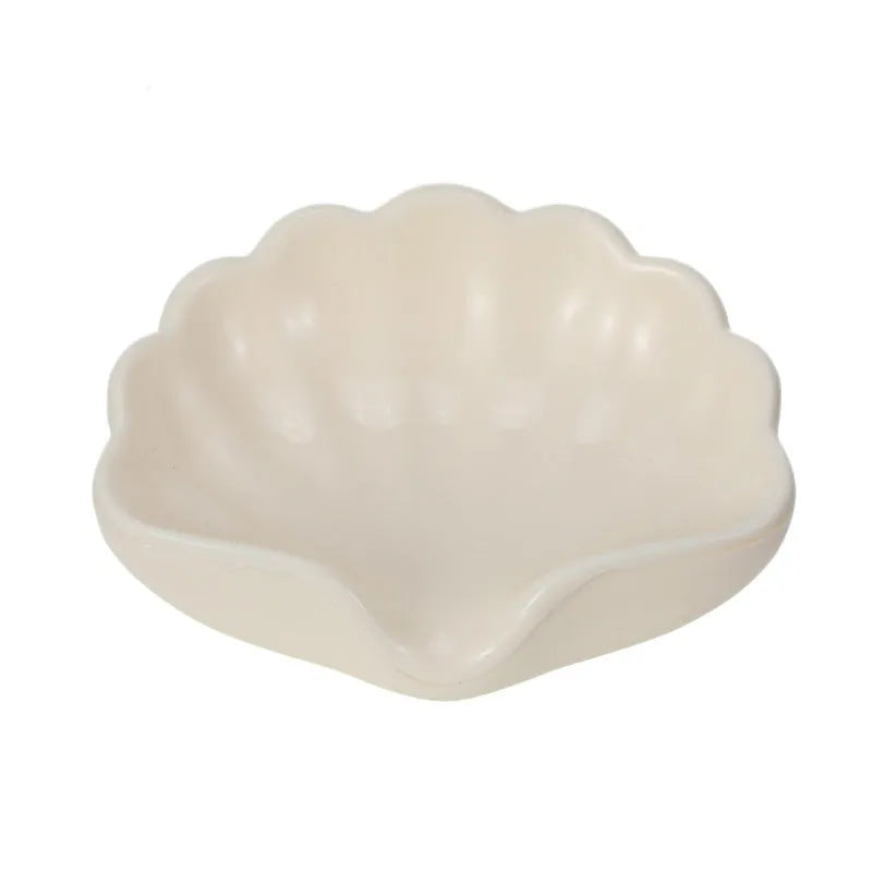 White plastic shell-shaped soap dish with a raised centre, placed on a bathroom counter.