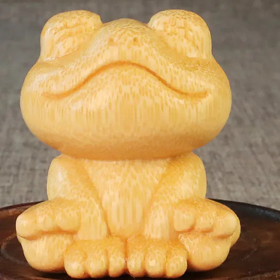Solid bamboo smiling frog carving ornament with cartoon style on a wooden surface.