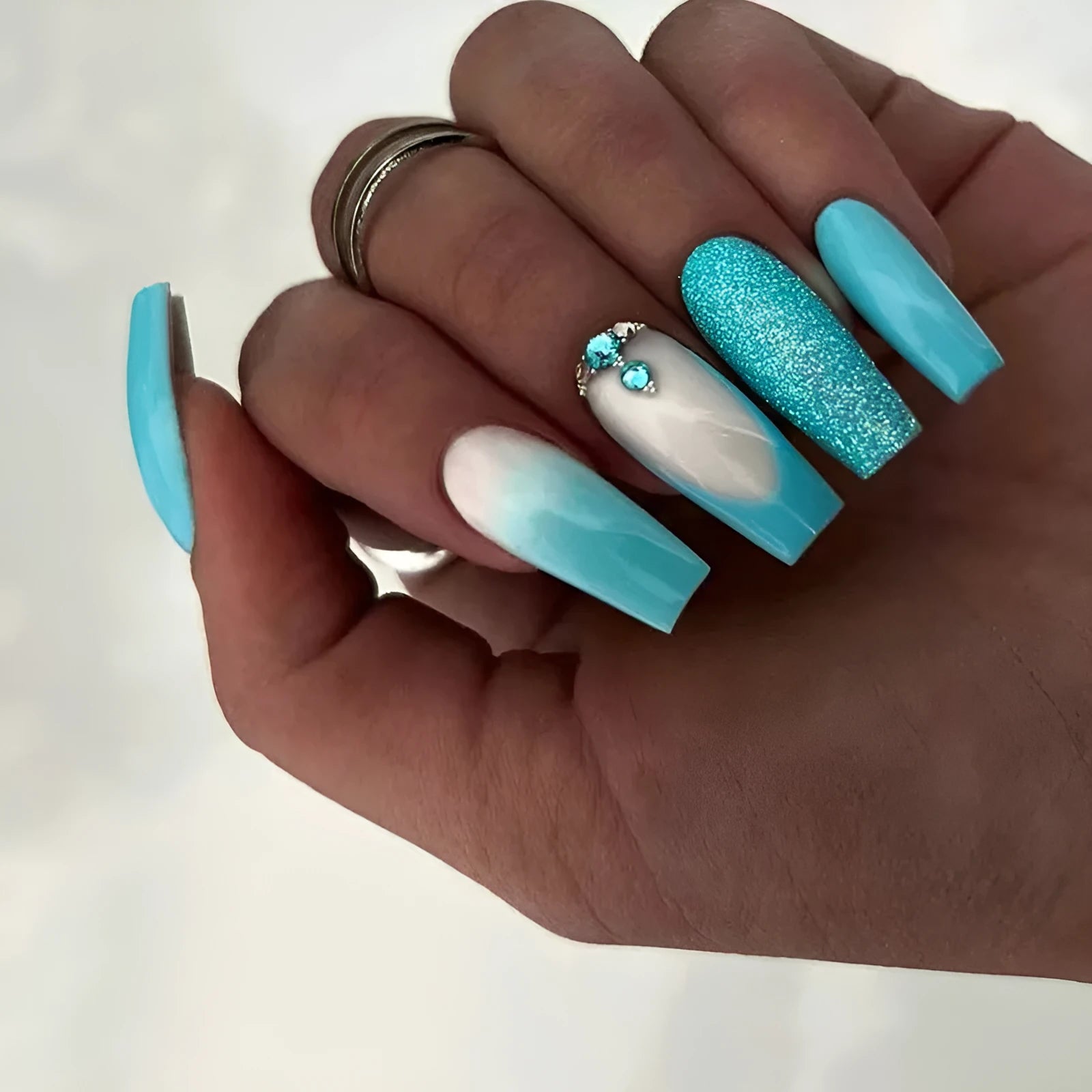 Long ballet-shaped false nails with solid blue colour and smart diamond glitter, shown with glue.