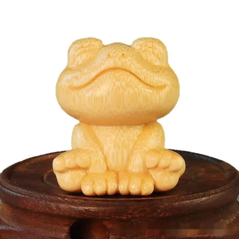 Solid bamboo smiling frog carving ornament with cartoon style on a wooden surface.