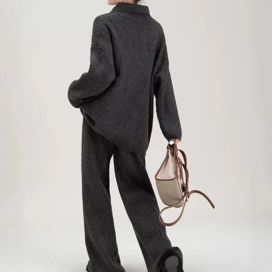 Dark gray knitted sweater and trousers two-piece set laid flat, showing long sleeves and elegant stitching details.