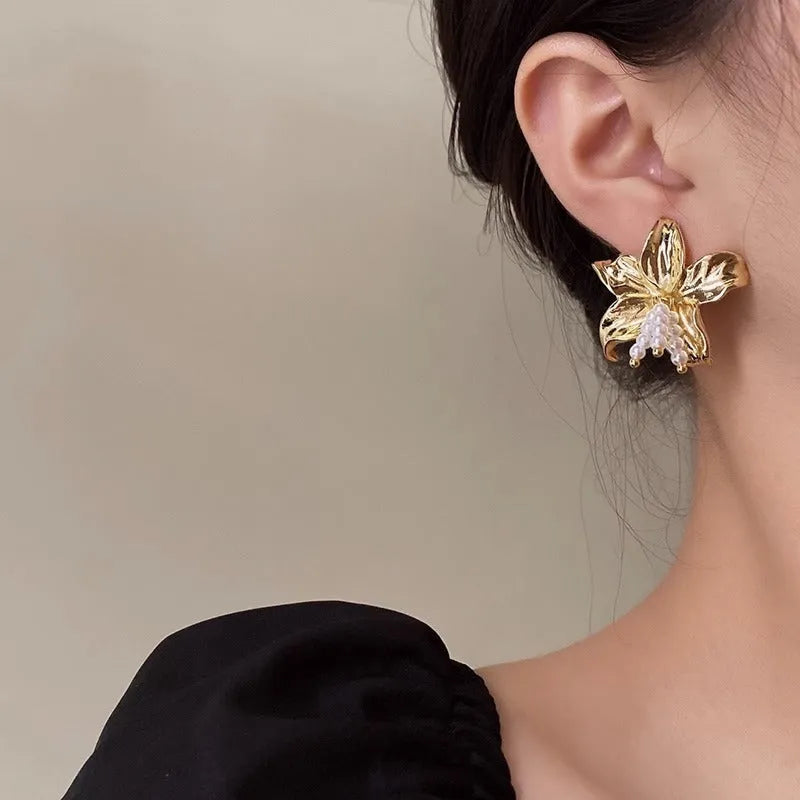 Gold pearl flower earrings with metal post back on white background, exaggerated floral shape
