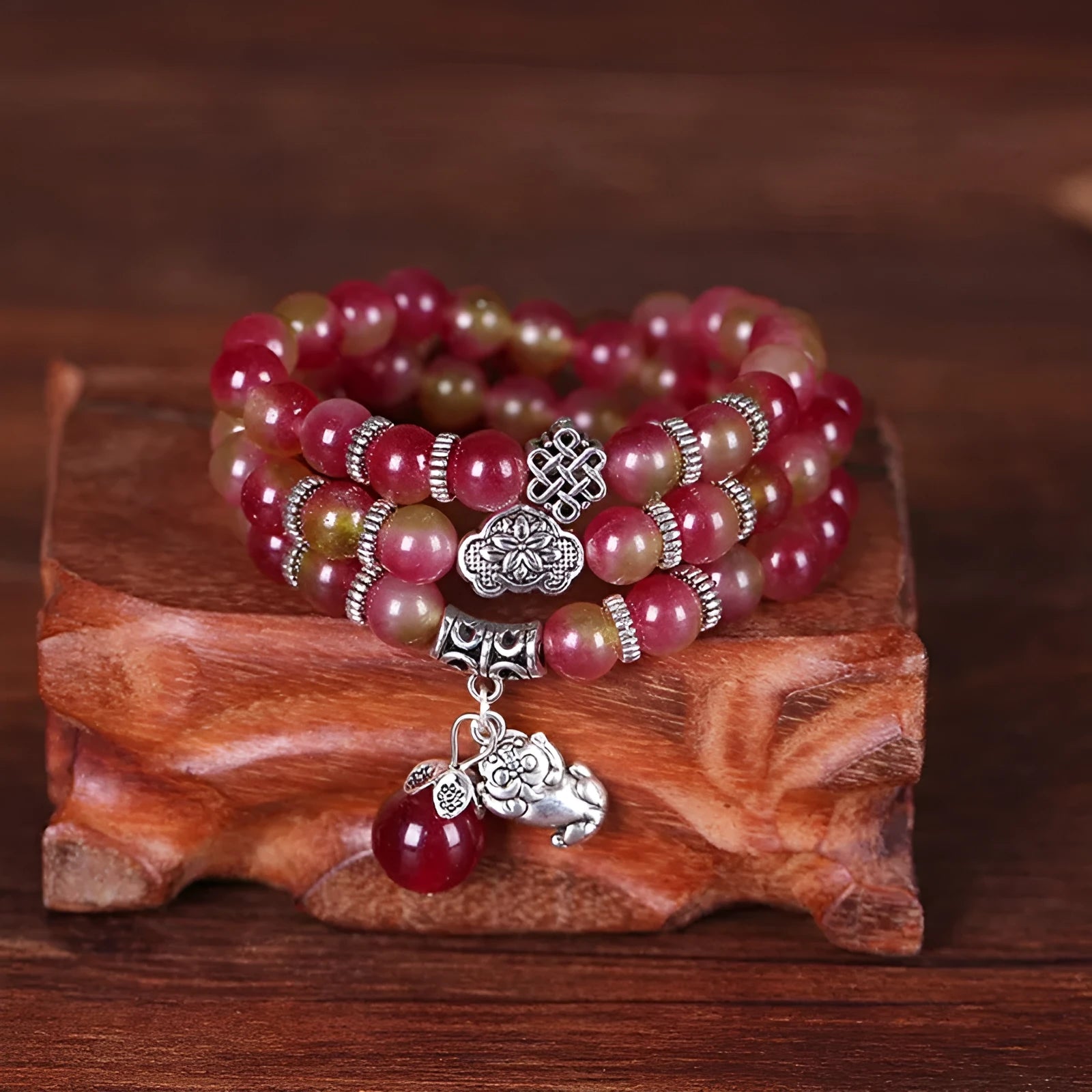 Close-up of a handmade watermelon crystal bracelet with a central Chinese knot and geometric beads.