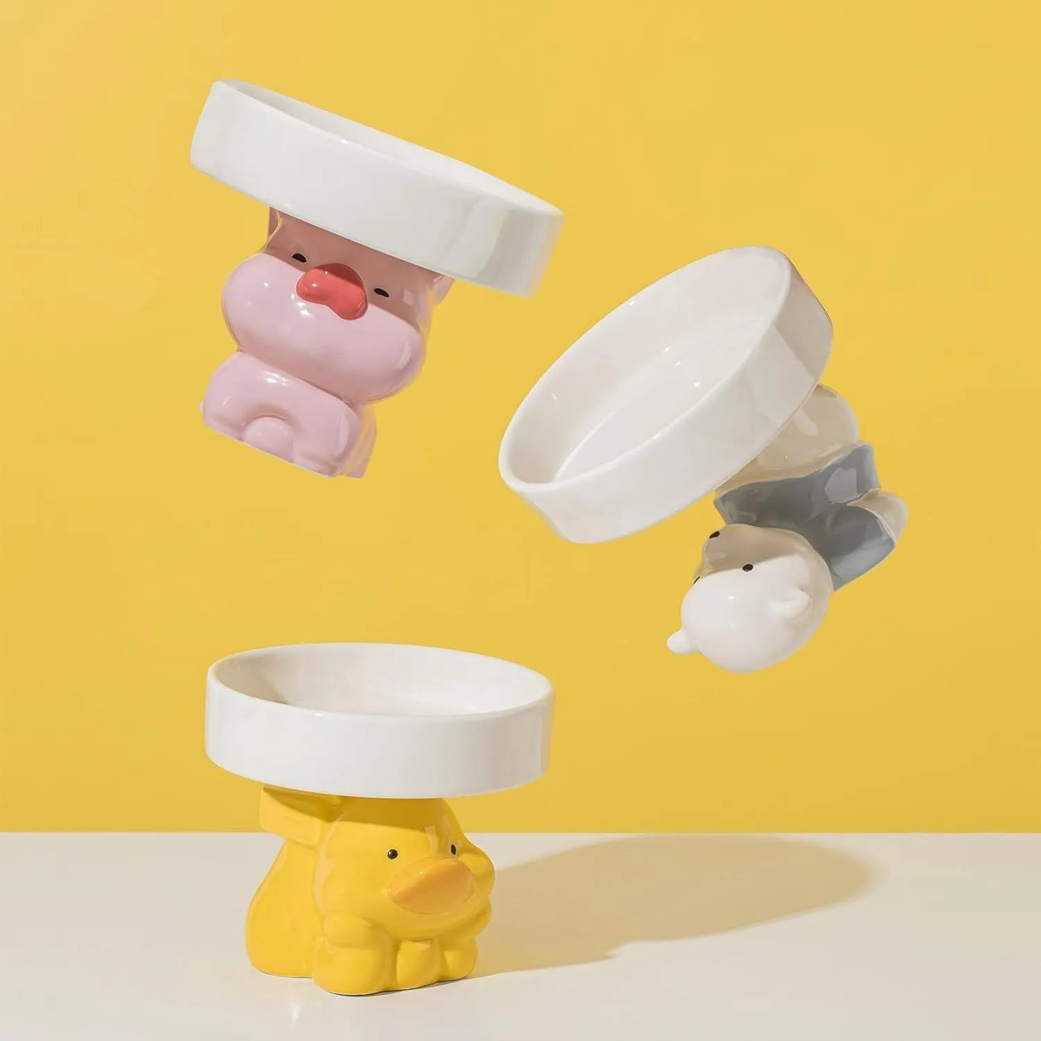 Raised ceramic cat bowl with animal design in pink, yellow, or white, showing wide feeding surface and elevated base.