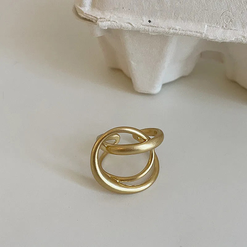 Geometric open ring for women with three-dimensional interlaced matte metal design in gold or silver.
