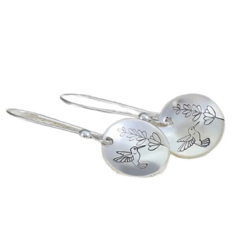 Silver-coloured round drop earrings with a detailed bird and floral design against leaves.