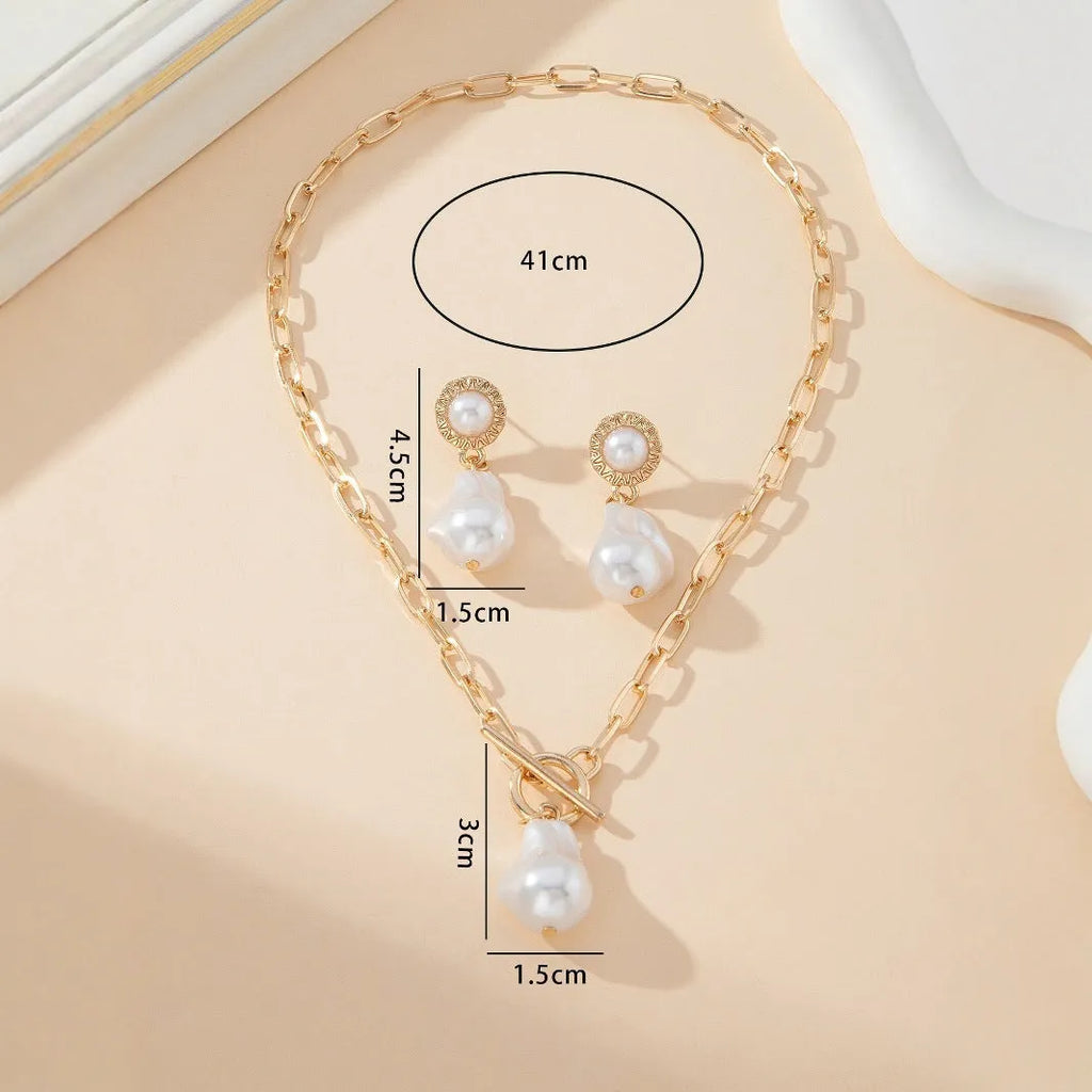 Gold retro baroque style necklace and earring set with pearl details on a white background.