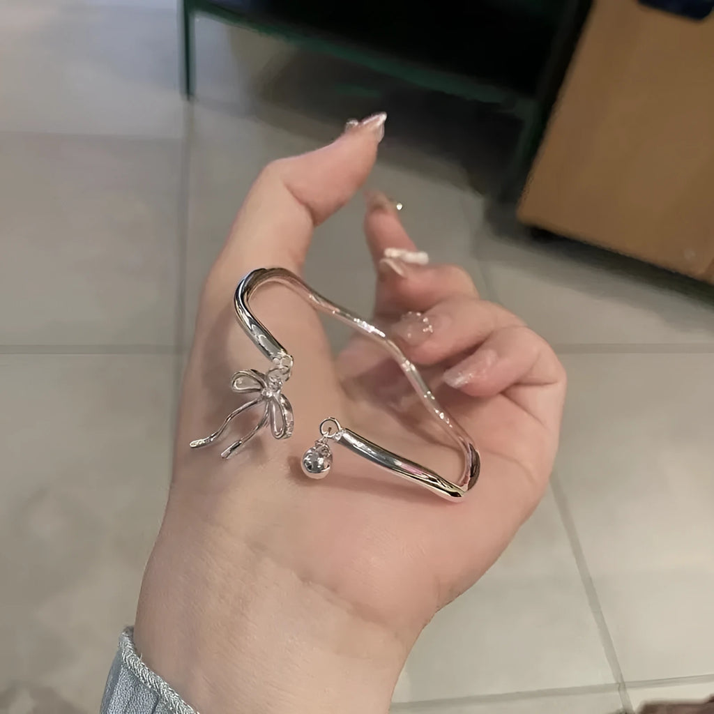 Silver tone adjustable bracelet with a bow and bell charm on a modelled wrist.