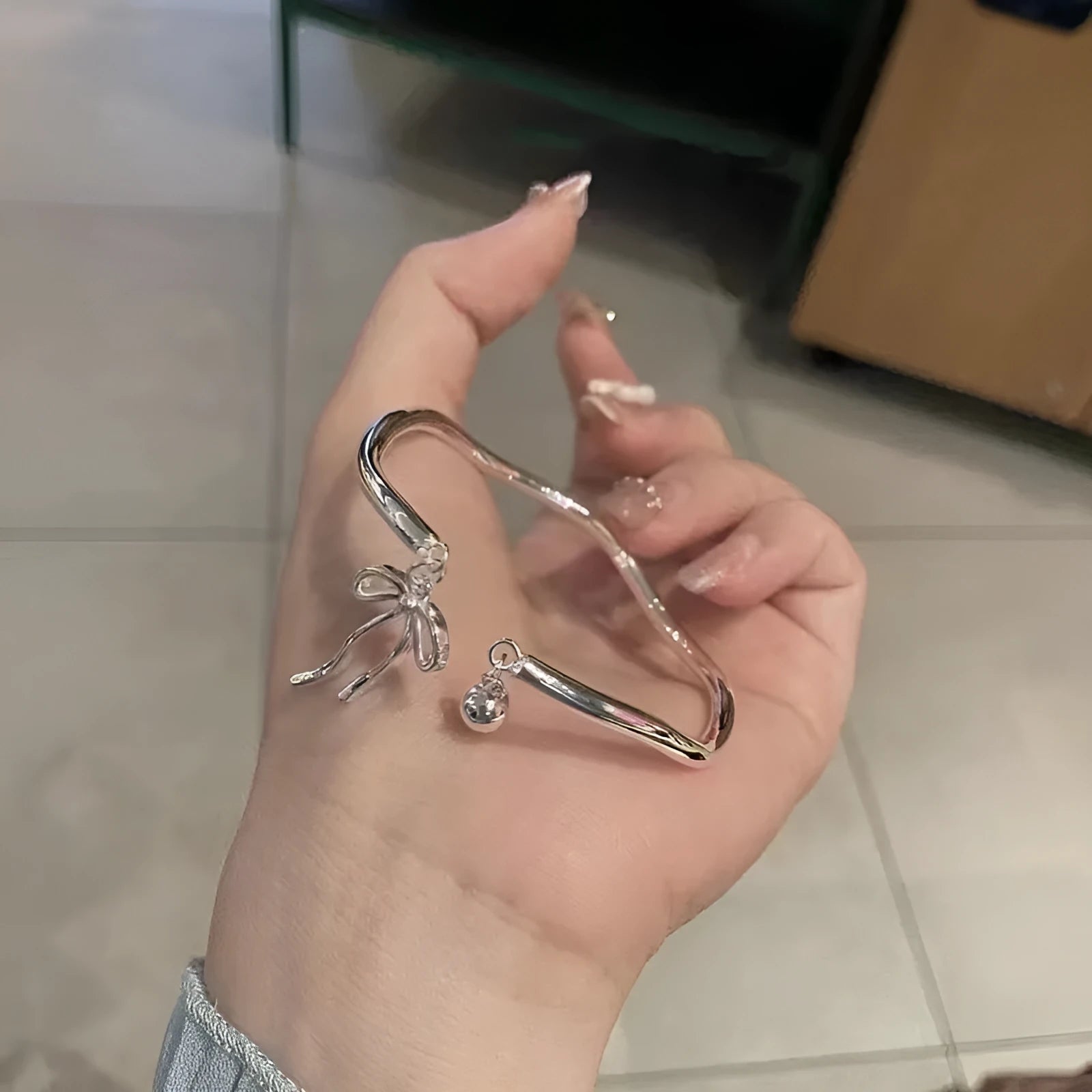 Silver tone adjustable bracelet with a bow and bell charm on a modelled wrist.