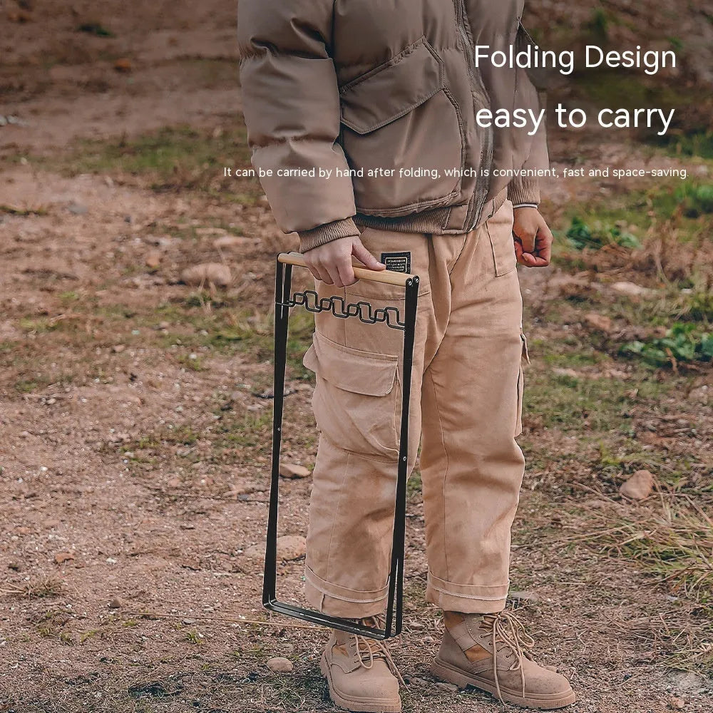 Black folding iron trash rack with a wooden handle holding a rubbish bag outdoors.