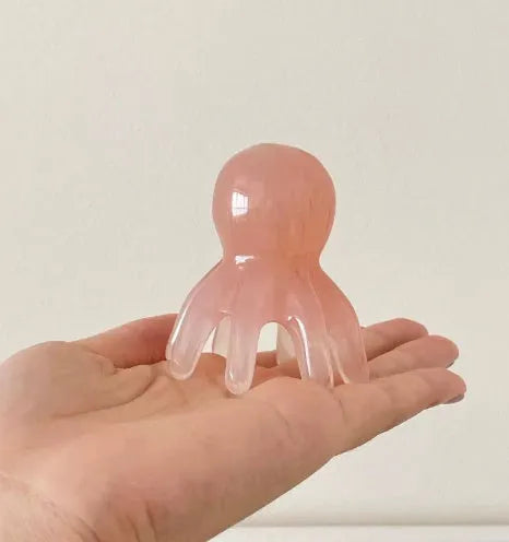 Pink octopus-shaped natural resin massage comb for periocular meridian, shown with its storage bag.