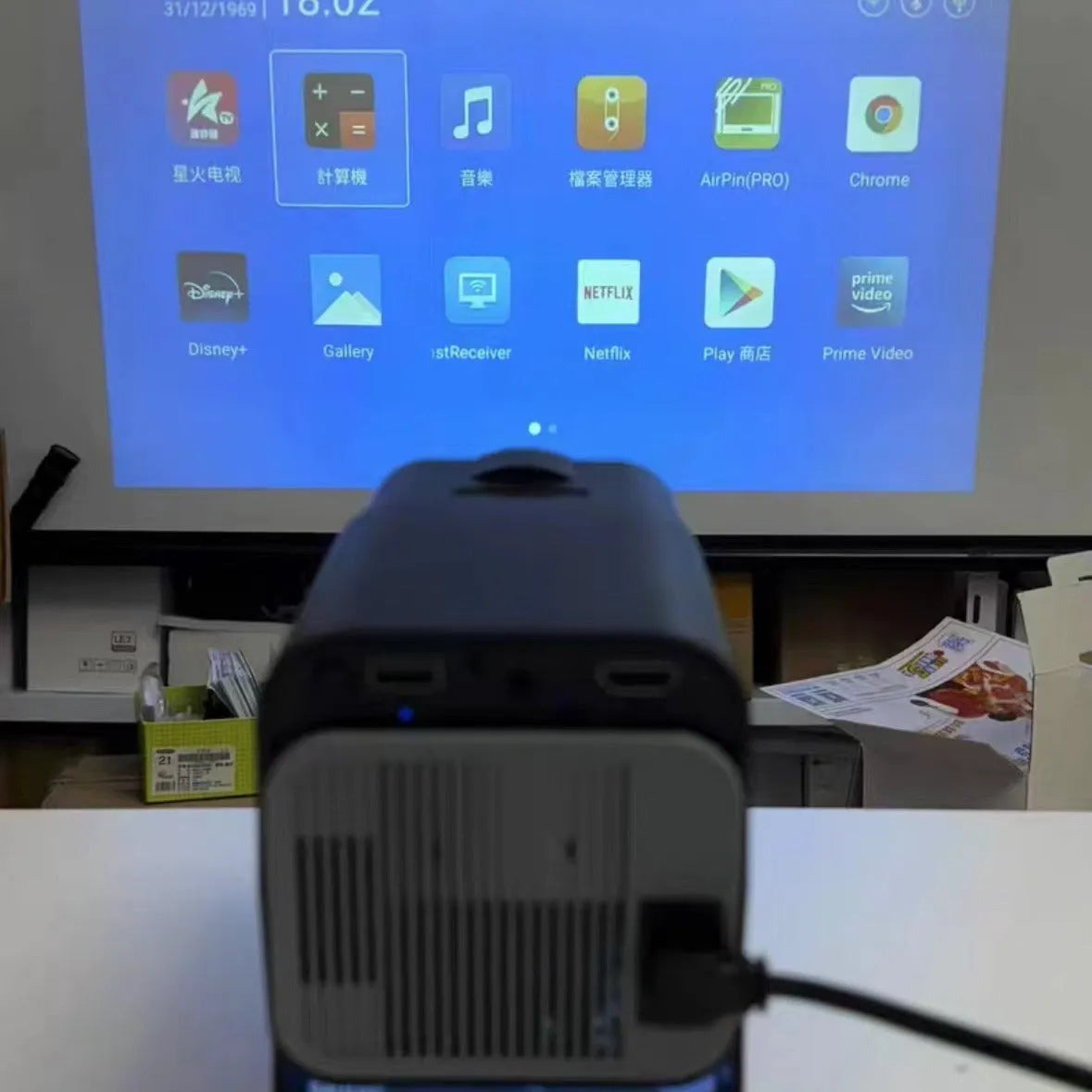 A white home projector unit on a wooden surface, showcasing its lens and wireless capabilities for HD projection.