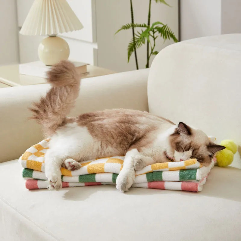 Green plaid pattern plush fleece pet blanket laid flat, showing soft texture and fur ball decoration.