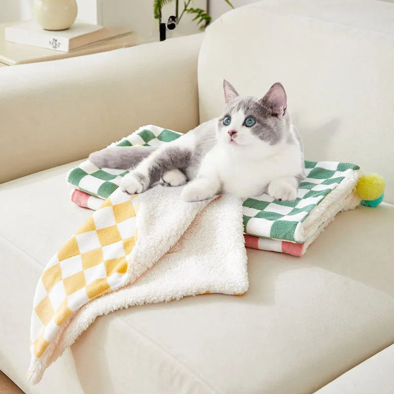 Green plaid pattern plush fleece pet blanket laid flat, showing soft texture and fur ball decoration.