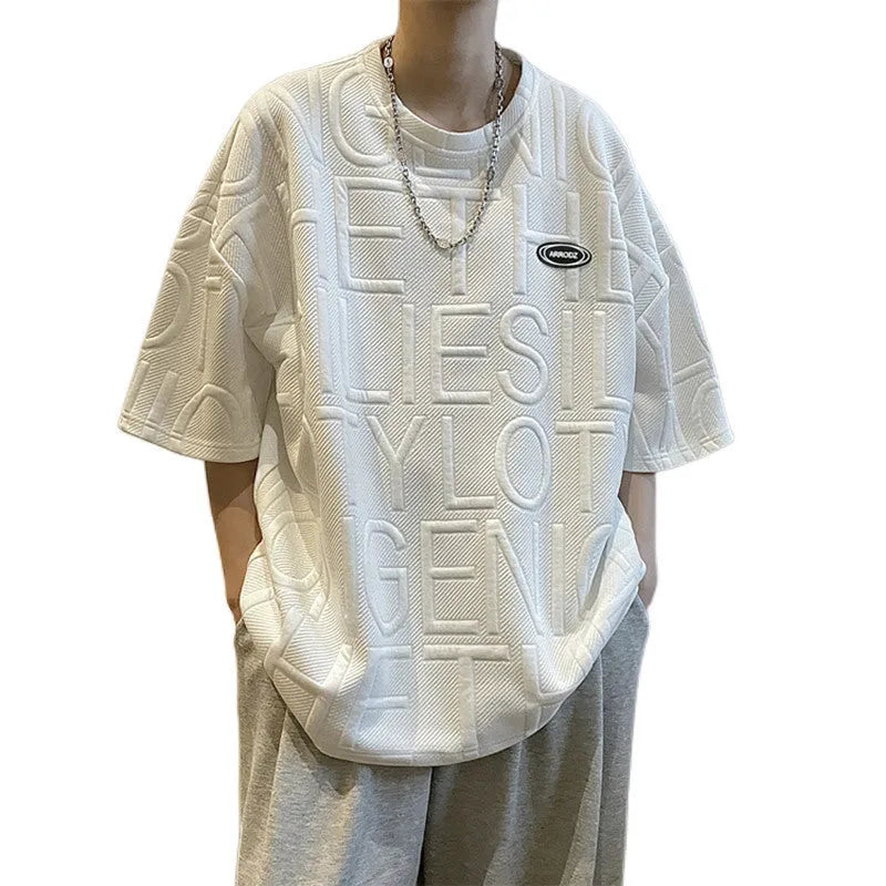 Man wearing a grey loose-fit t-shirt with a retro-style three-dimensional raised letter graphic on the front.