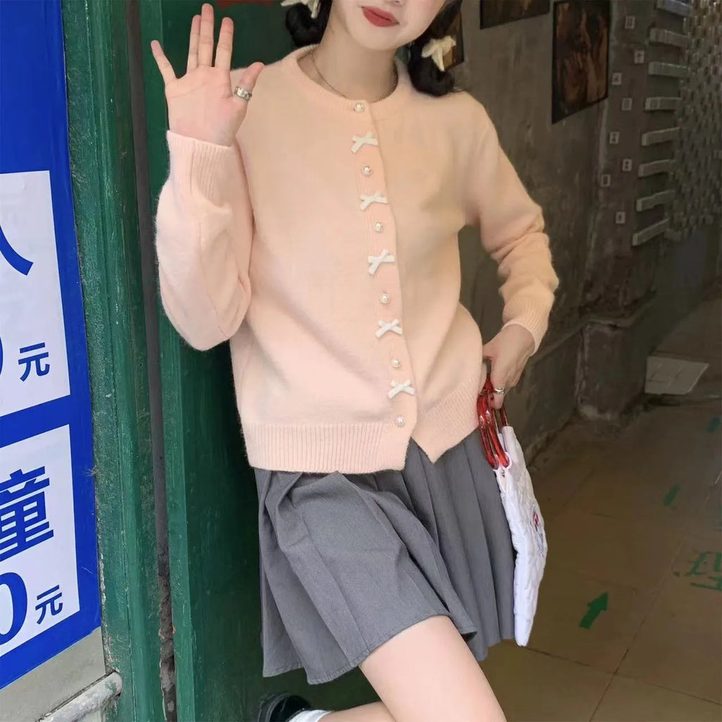 Women's cardigan sweater with a decorative bow and pearl buttons, shown in a solid colour.