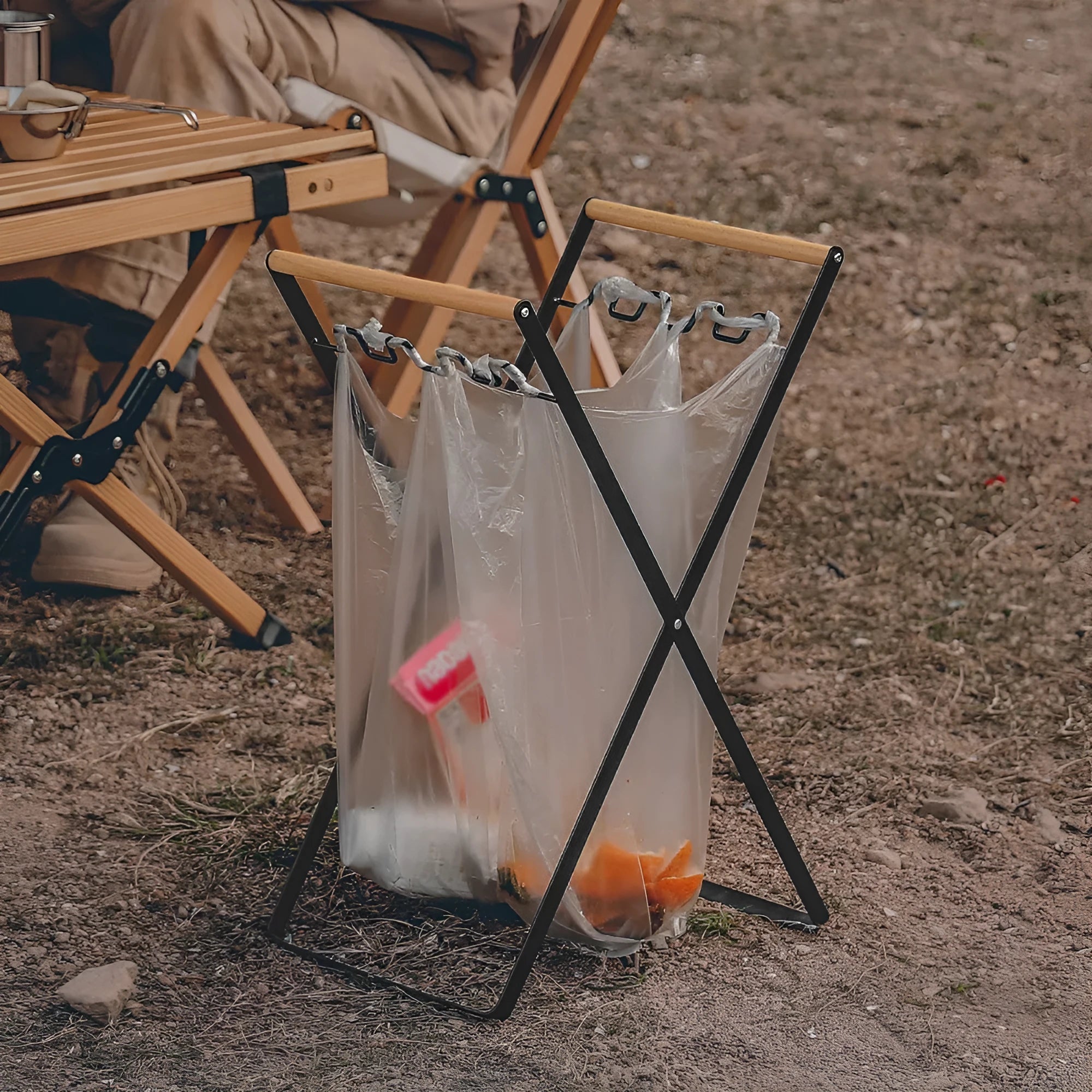 Black folding iron trash rack with a wooden handle holding a rubbish bag outdoors.