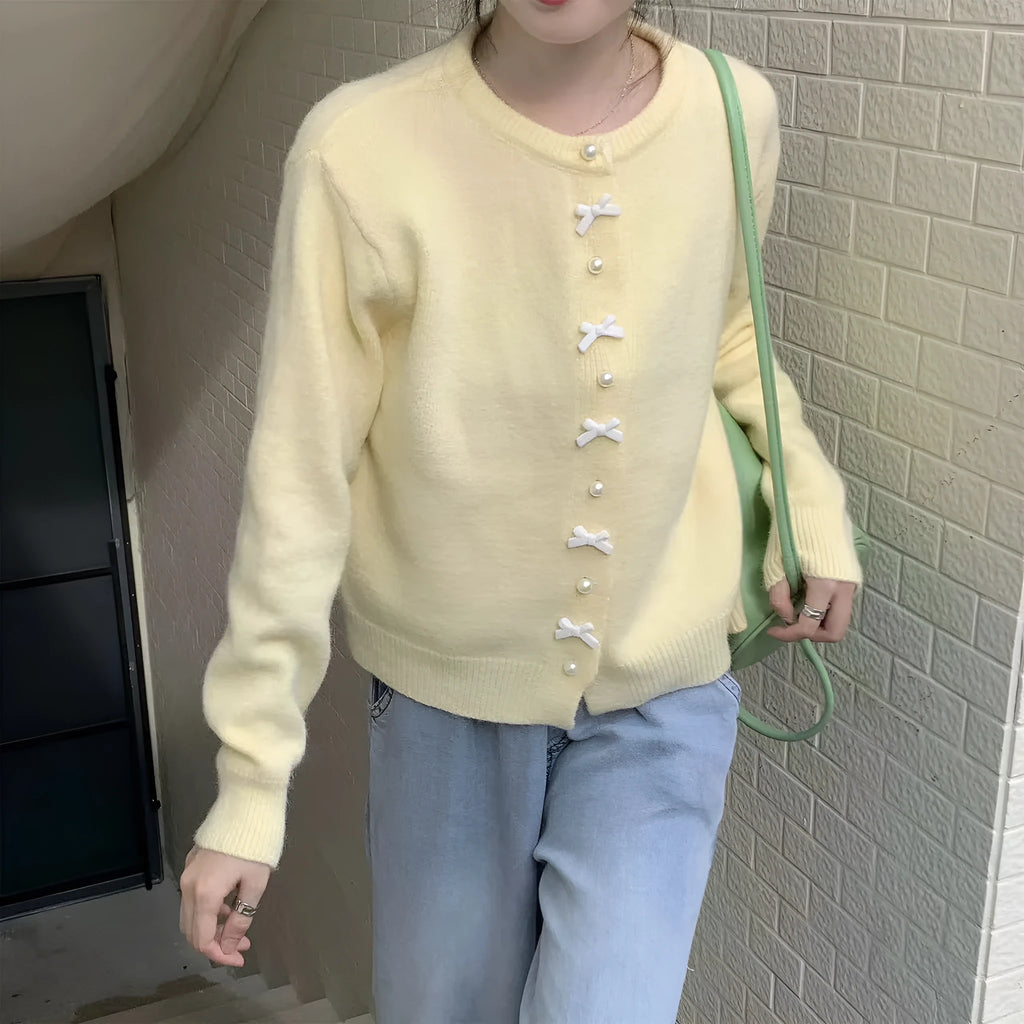 Women's cardigan sweater with a decorative bow and pearl buttons, shown in a solid colour.
